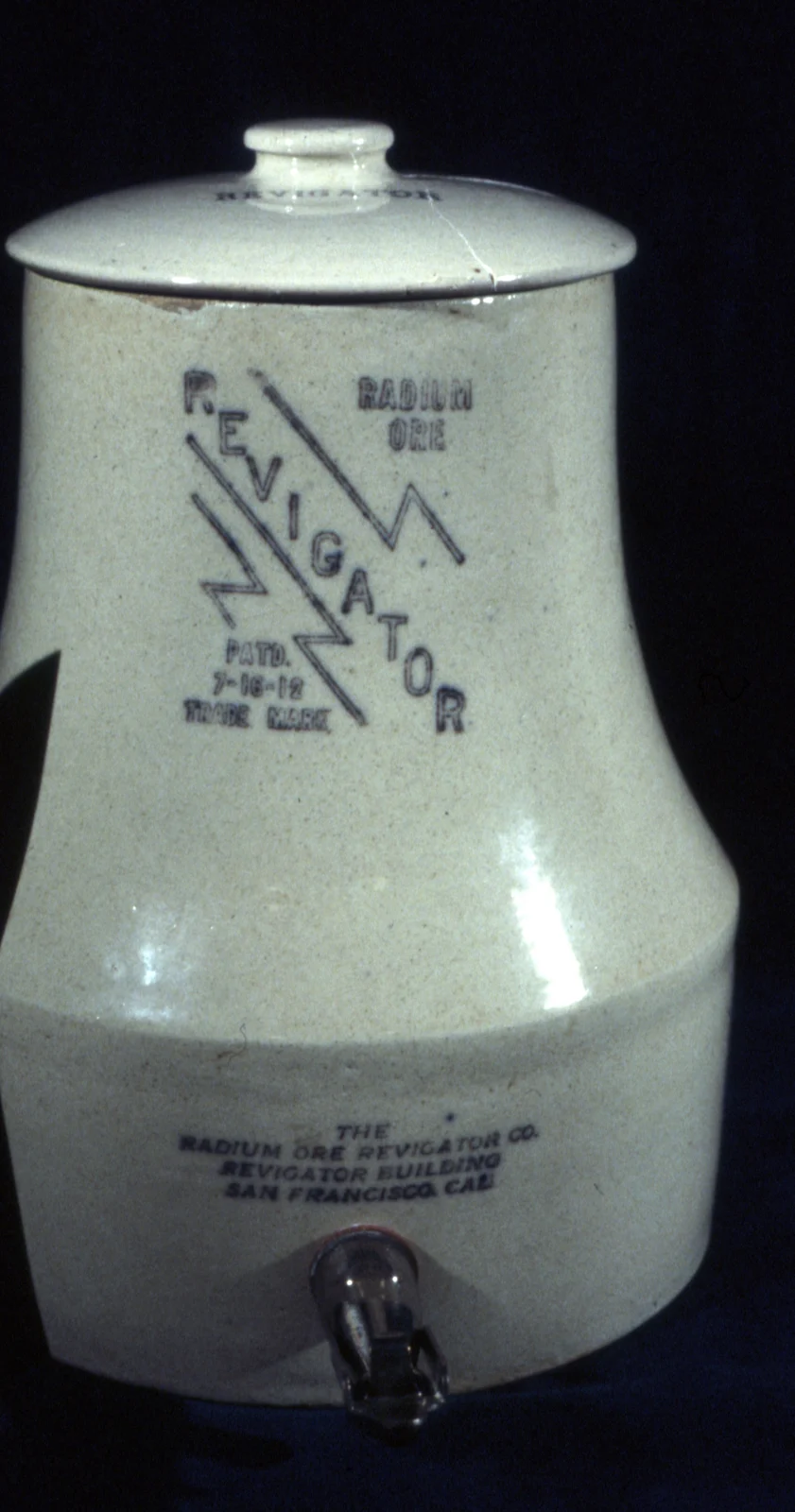 A pale stoneware water crock with a lid and a spigot, stamped Radium Ore Revigator with a lightning-shaped mark.