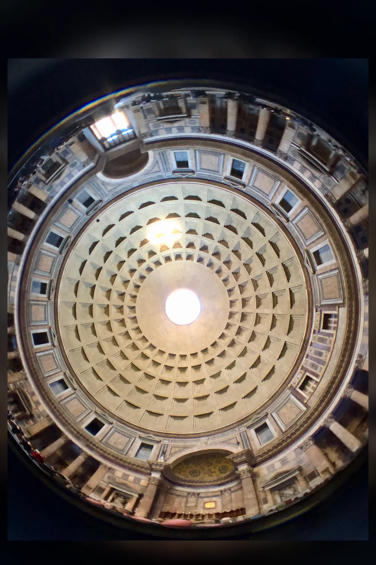 The inside of the Pantheon dome seen straight up through a wide lens: rings of square recessed coffers narrowing to a bright round opening at the top, ringed by the drum and its windows.