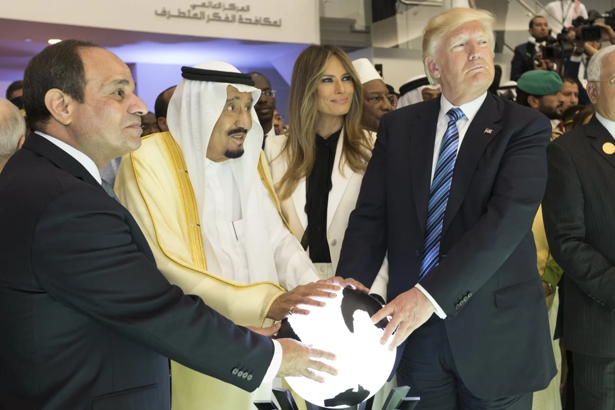 Three men with their hands on a lit globe, Melania Trump beside them, in a dark room.