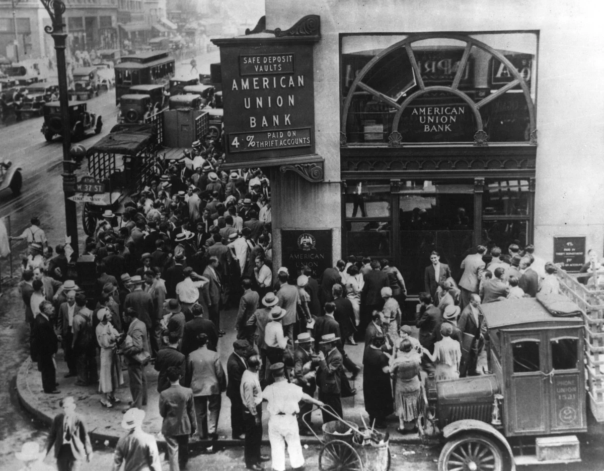 A dense crowd of people in coats and hats fills the street outside a bank.