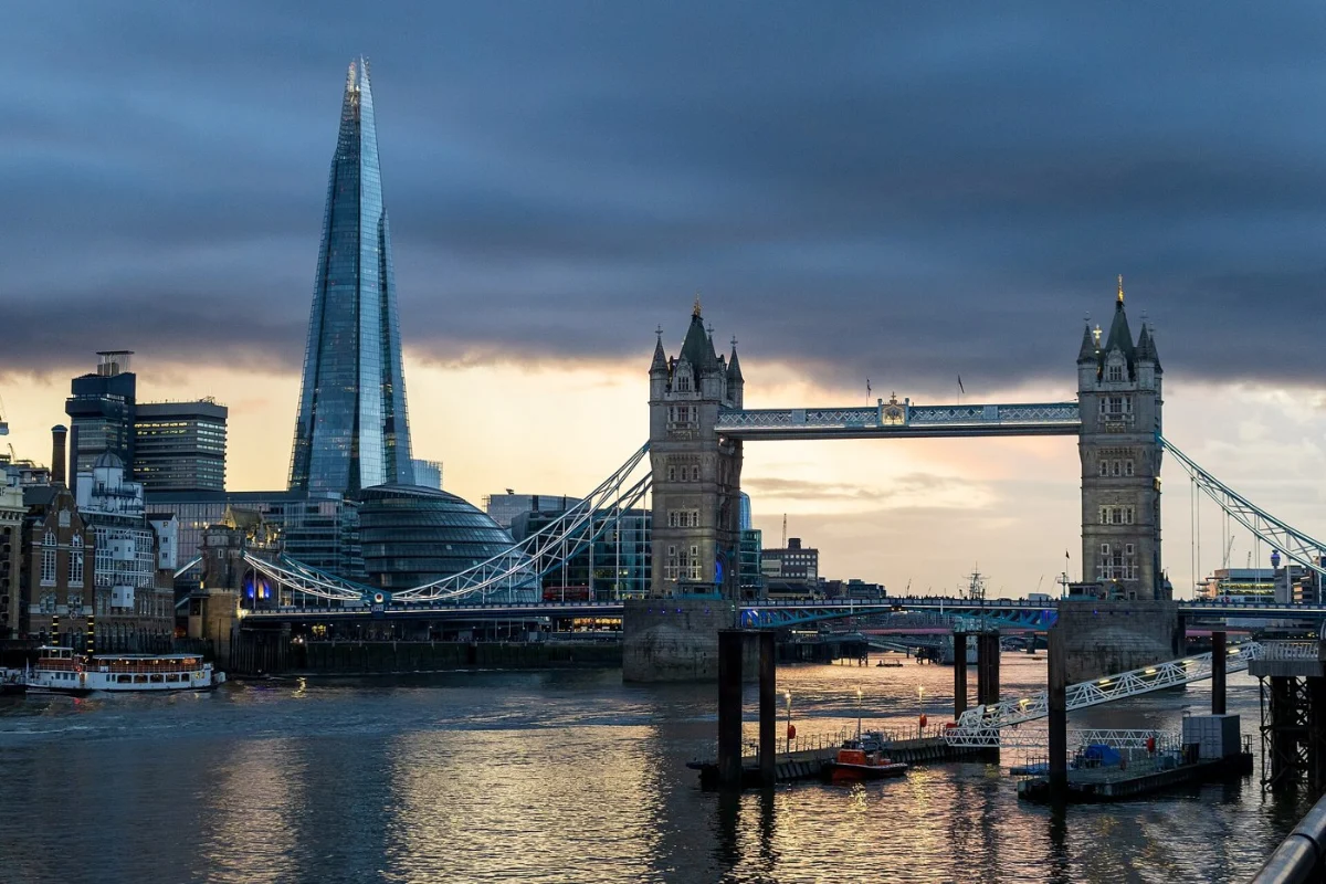 A tall glass spire rising behind Tower Bridge across the Thames at dusk.