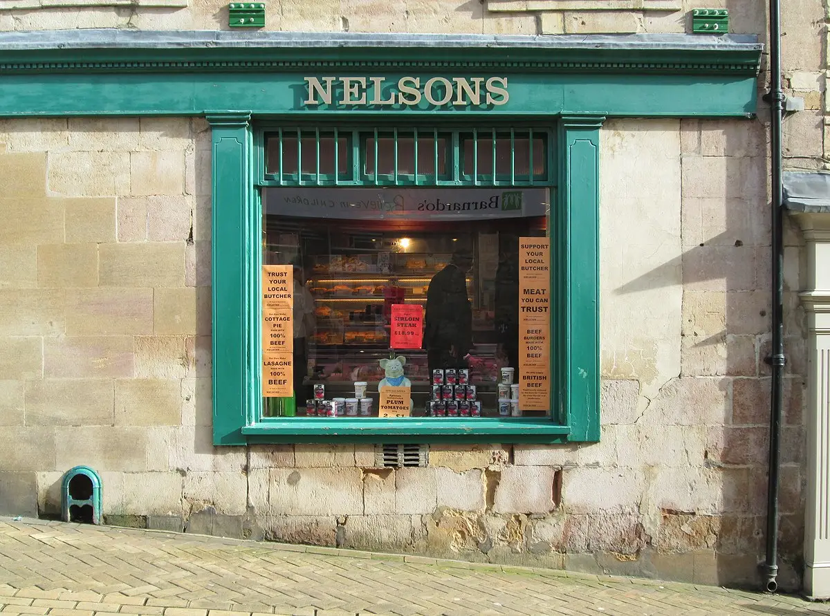 A butcher's shop window with handbills telling customers its pies and burgers are pure beef.