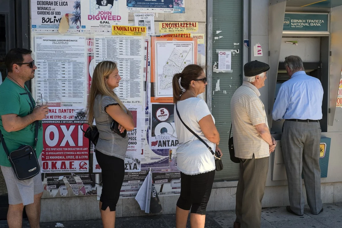 People queuing at a bank cash machine, with posters on the wall beside them.