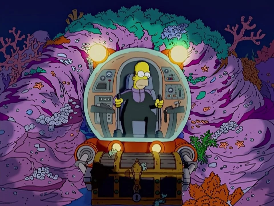 Homer sitting in a round glass submersible wedged in coral on the sea bed, a treasure chest beside him.