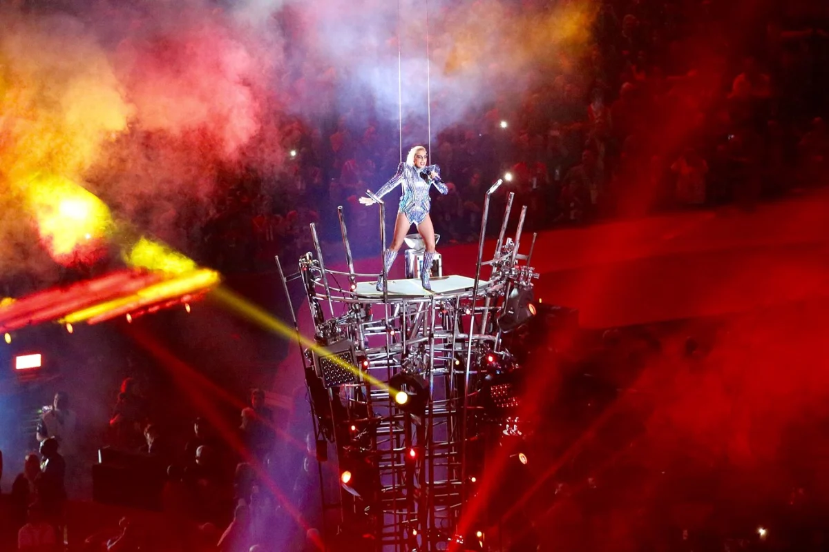 Lady Gaga high on a tall stage structure in smoke and flame.