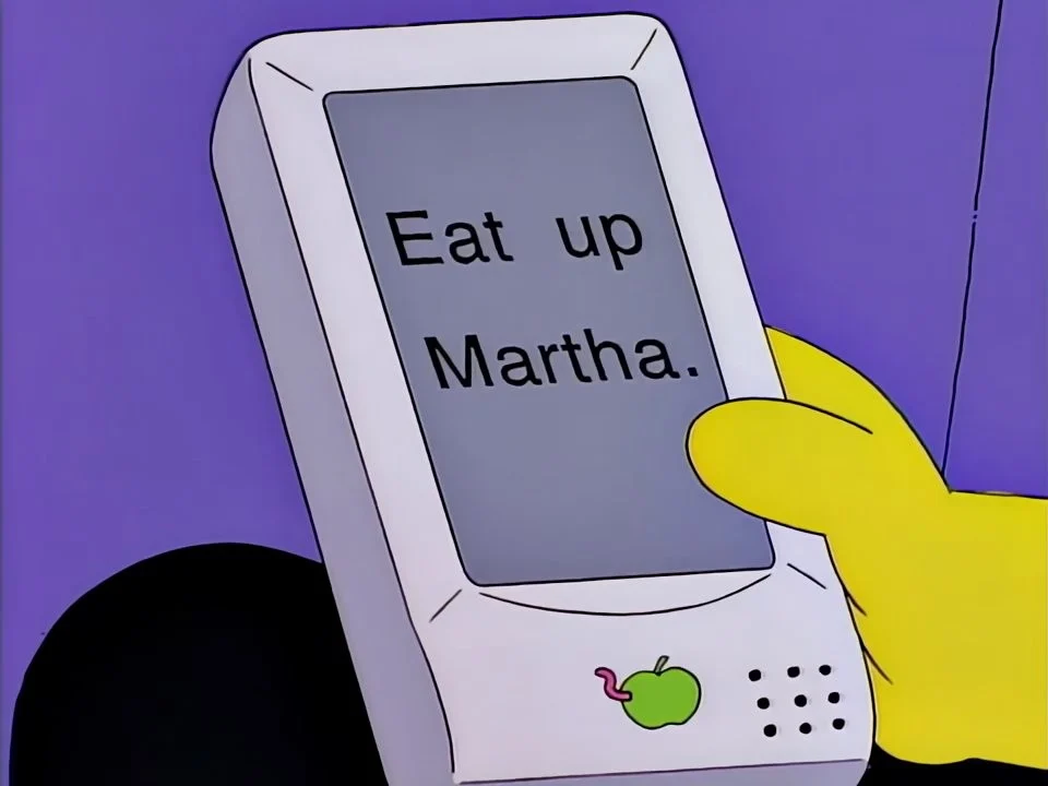 A hand holding a pale grey tablet whose screen reads Eat up Martha.