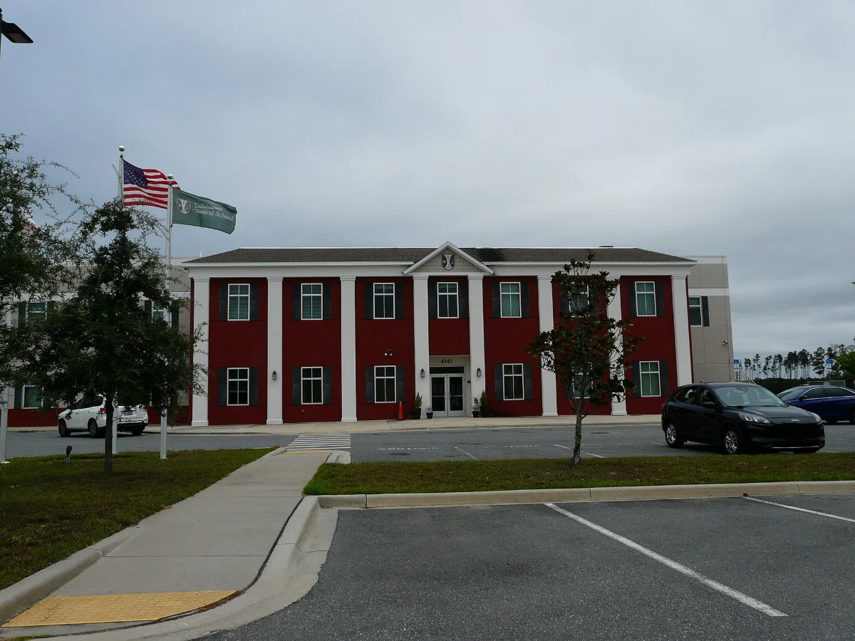 A two-storey red and white school building with a flag, beside a car park.