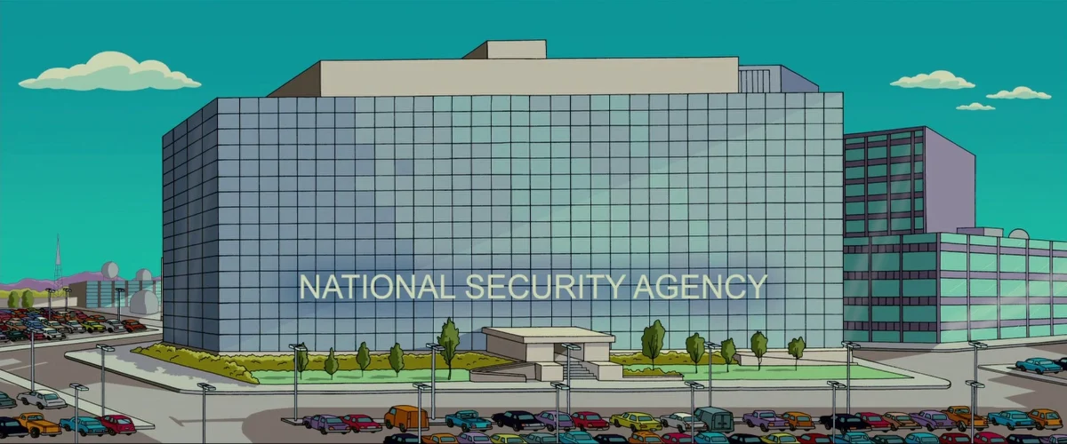 A large glass cube labelled National Security Agency, with parked cars and radar domes behind.