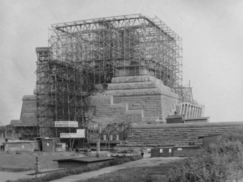 A large stone structure under construction with timber scaffolding around its upper part.