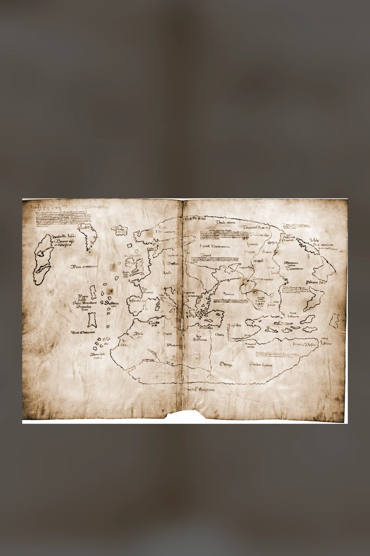 The Vinland Map: faint brown outlines of Europe, Africa and Asia on pale folded parchment, with a large island labelled Vinlanda Insula at the far left, west of Greenland.