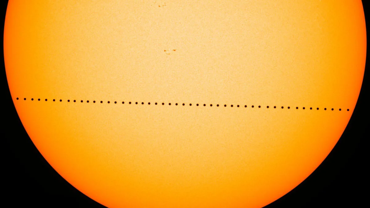 The orange disc of the Sun crossed by a line of small black dots, the positions of Mercury during its transit