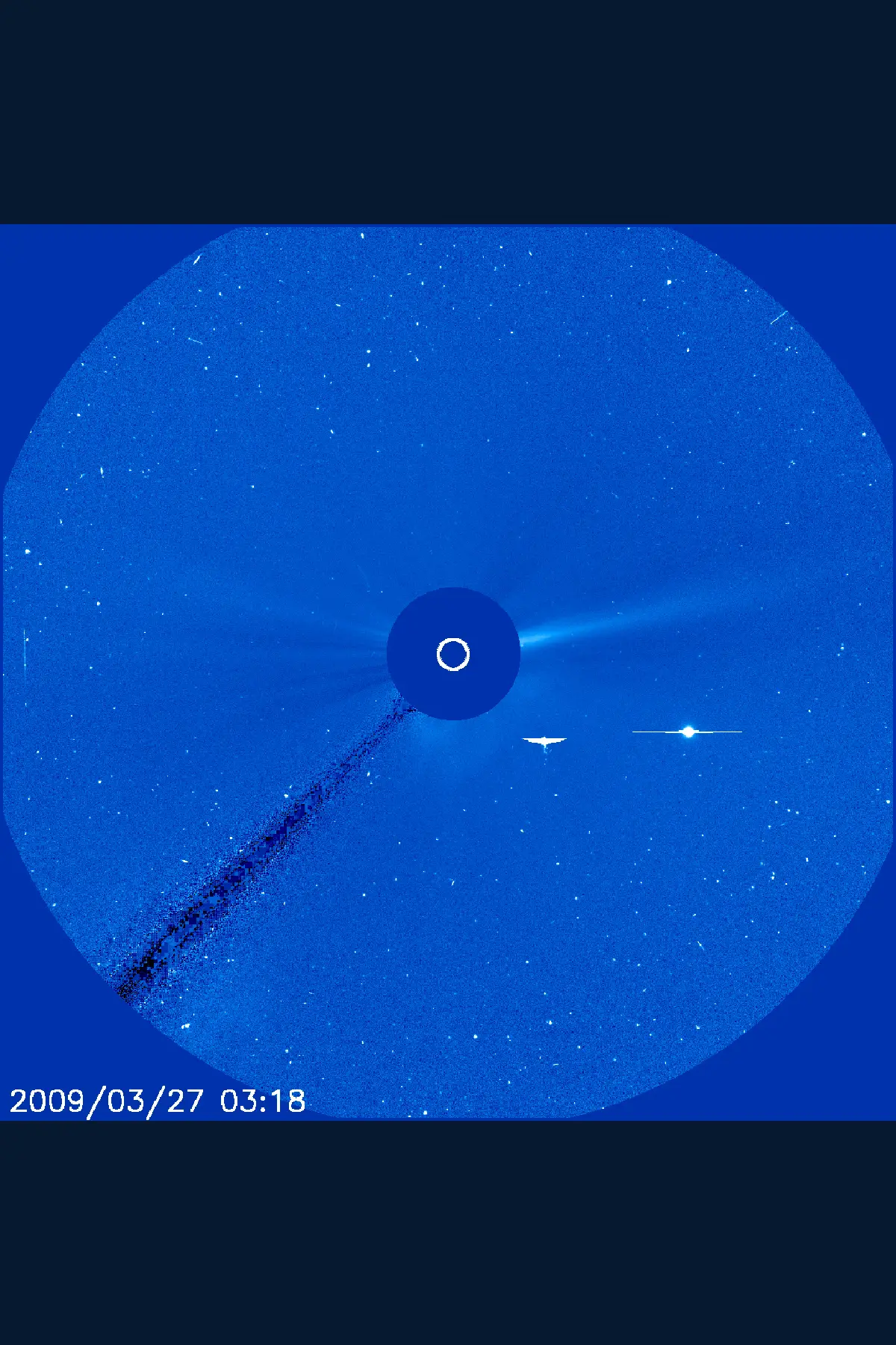 Full blue LASCO C3 field with an occulting disk, wing-shaped white mark, and separate bright point to its right.