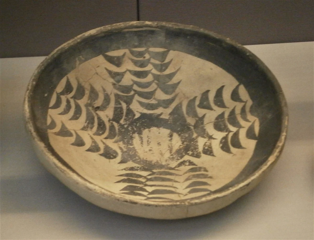 A shallow pale clay bowl painted inside with rows of dark curved brush strokes.