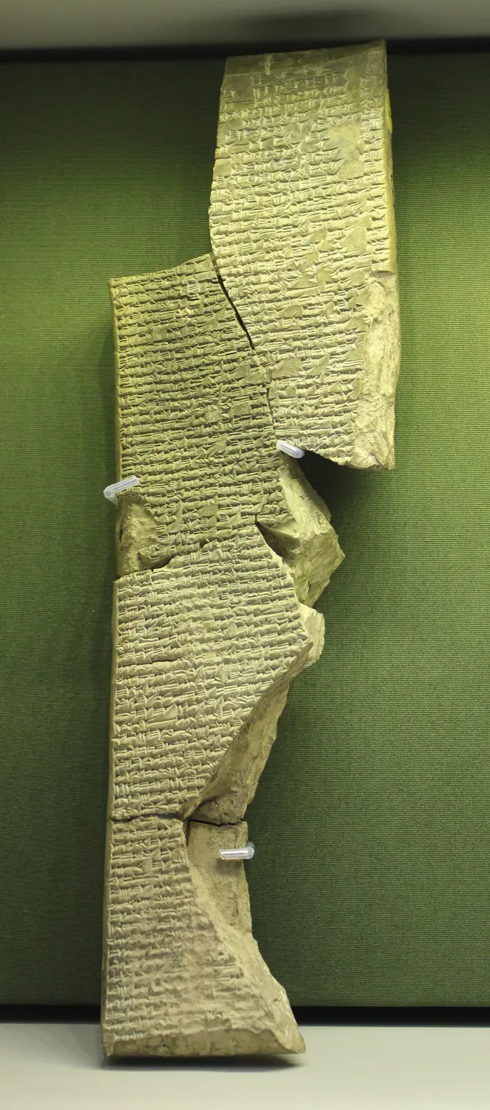 A tall fragment of a clay tablet, broken on all sides, covered in rows of small wedge-shaped cuneiform signs.
