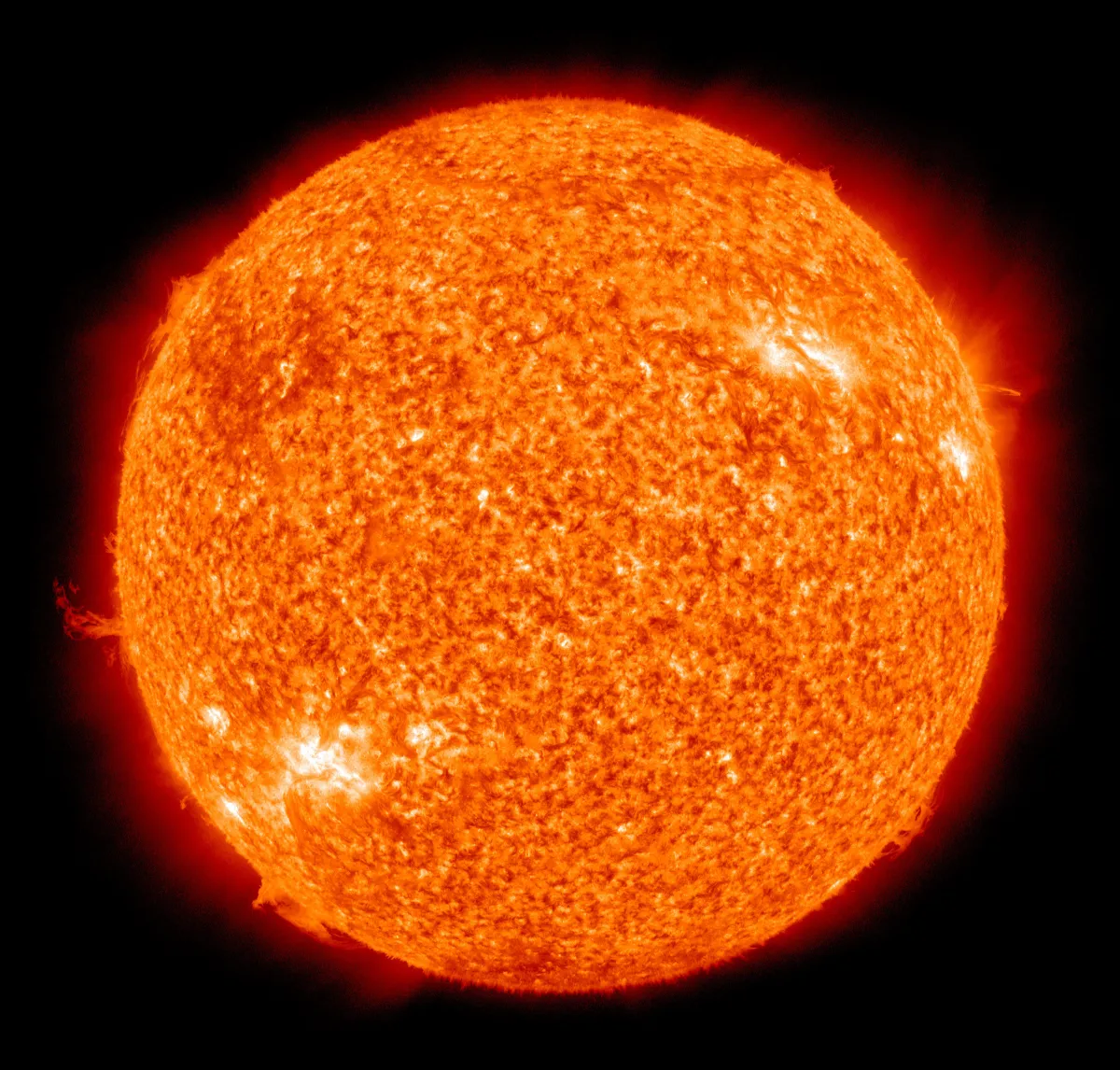 The full disc of the Sun in false-colour orange, mottled and bright at the edges, with loops of glowing gas at the rim, on a black background.
