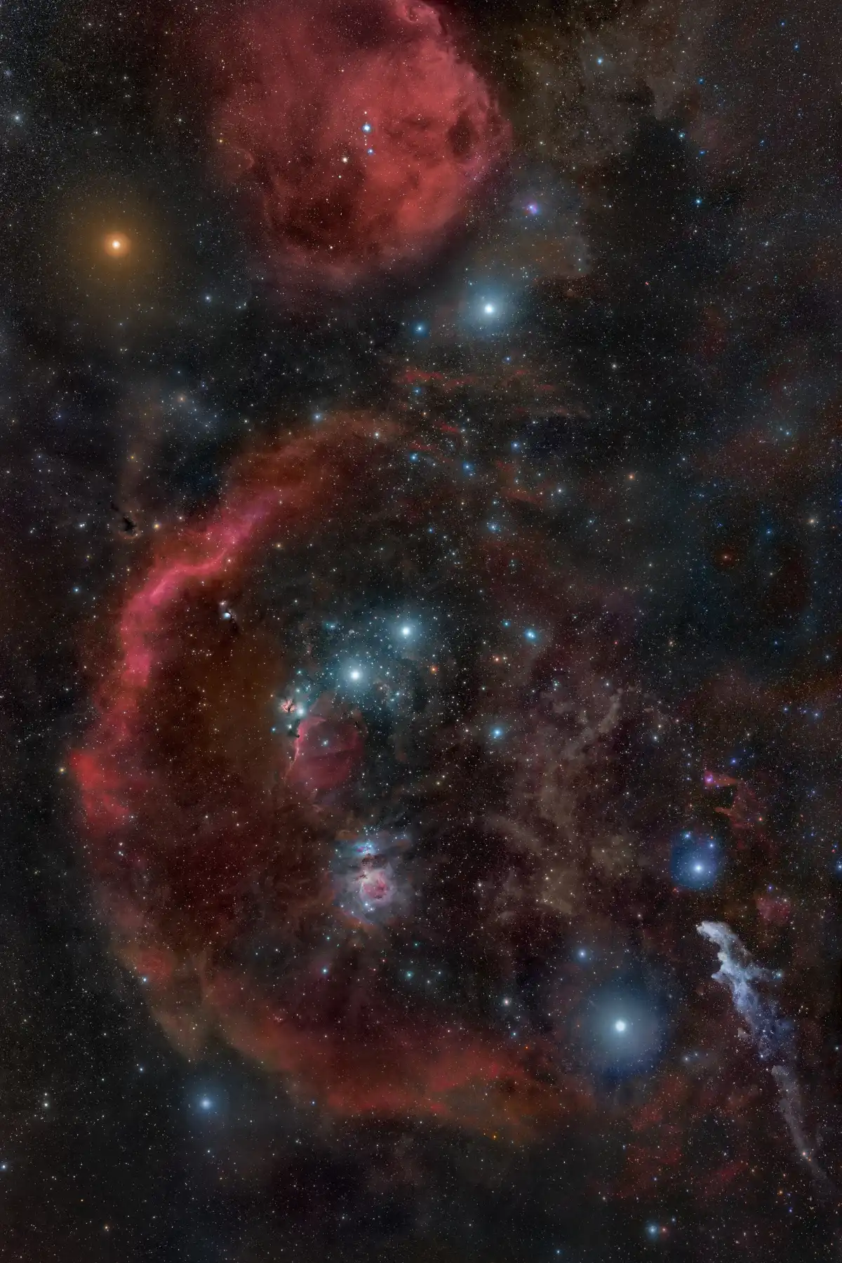 The constellation Orion across a deep star field: the red arc of Barnard's Loop, the three belt stars in a diagonal line, the glowing Orion Nebula below them, red Betelgeuse at upper left and blue-white Rigel at lower right.