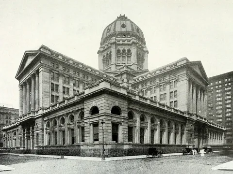 Black and white photo of the huge stone building from a street corner: a tall octagonal drum and ribbed dome over pedimented wings, with arched windows below.