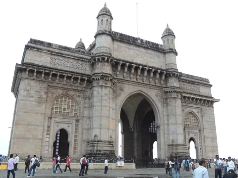 A massive basalt triumphal arch with four corner turrets and lattice windows, seen at a slight angle, with visitors on the plaza in front.