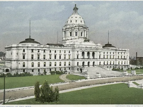 Postcard of the white marble Capitol seen across lawns: a long classical front, a large white dome on a drum, smaller dark domes at the ends and a broad stair.