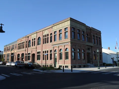 A two-storey red brick civic building on a street corner, with pale stone bands and arched windows, and a longer wing running back from the corner.