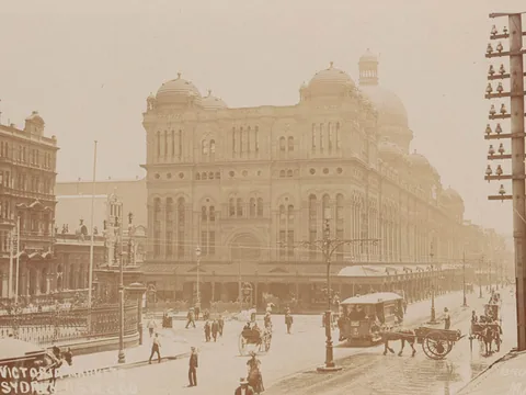 Sepia postcard of a domed stone market building filling a street corner, with a horse tram, carts and pedestrians, and a tall telegraph pole at right.