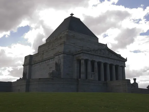 Colour photograph of a grey stone memorial with a stepped pyramid roof above a columned portico, on a grassy rise under broken cloud.