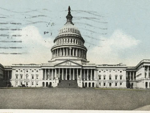 Postcard view of the Capitol from the east: long white front, central cast-iron dome, a pedimented wing at each end and a wide empty plaza before it.