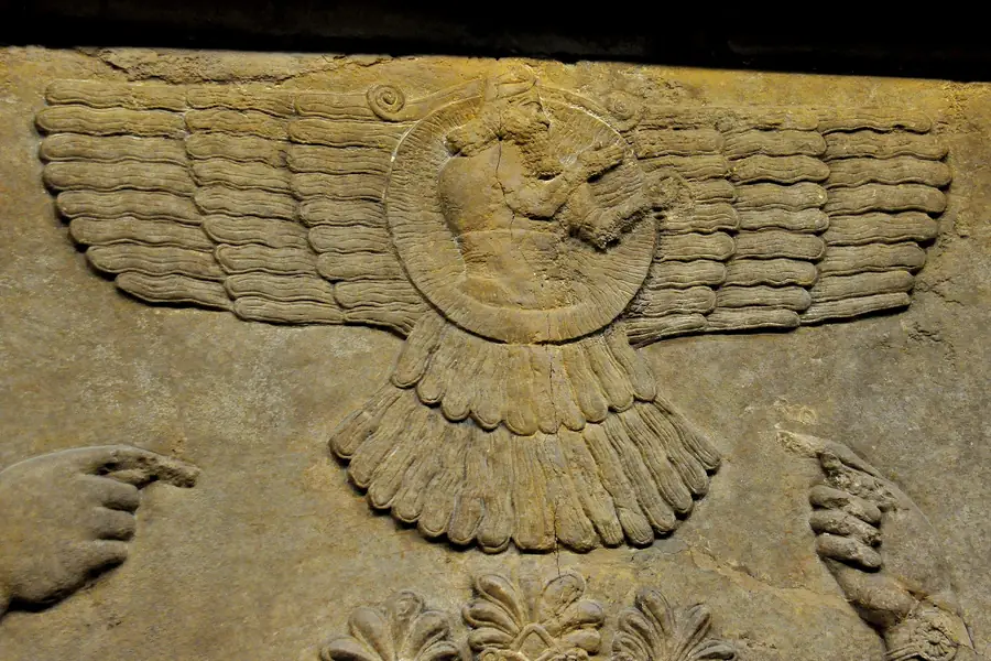 A stone relief of a bearded figure inside a disc with wide feathered wings and a feathered tail.